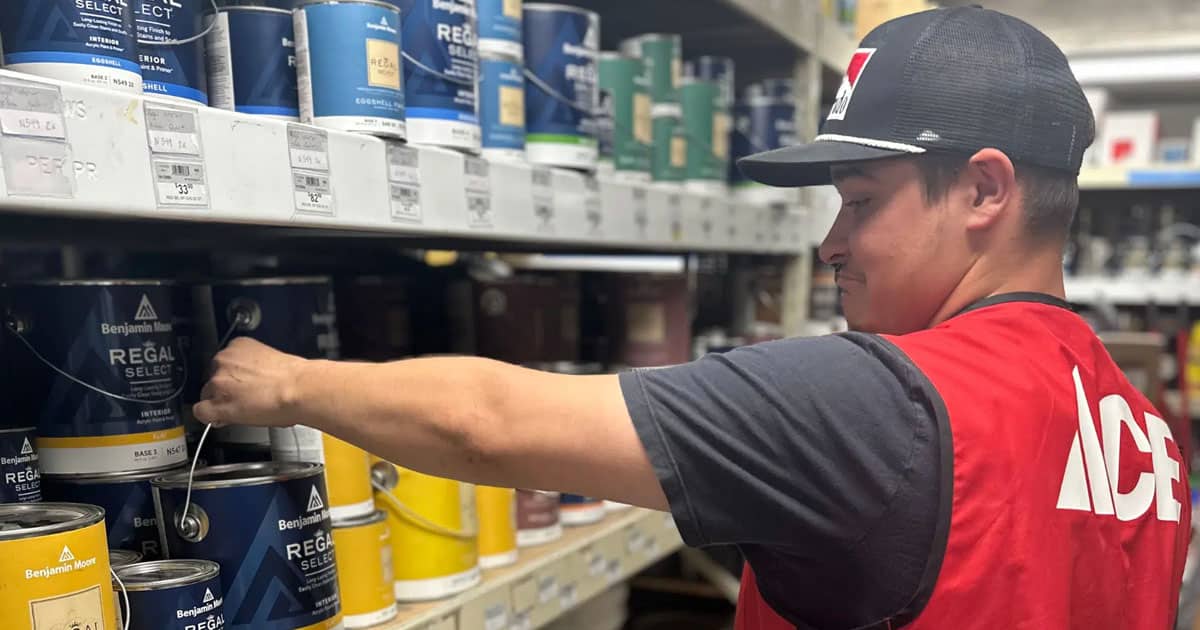 Timberline Ace Hardware employee stacking cans of paint on the shelves