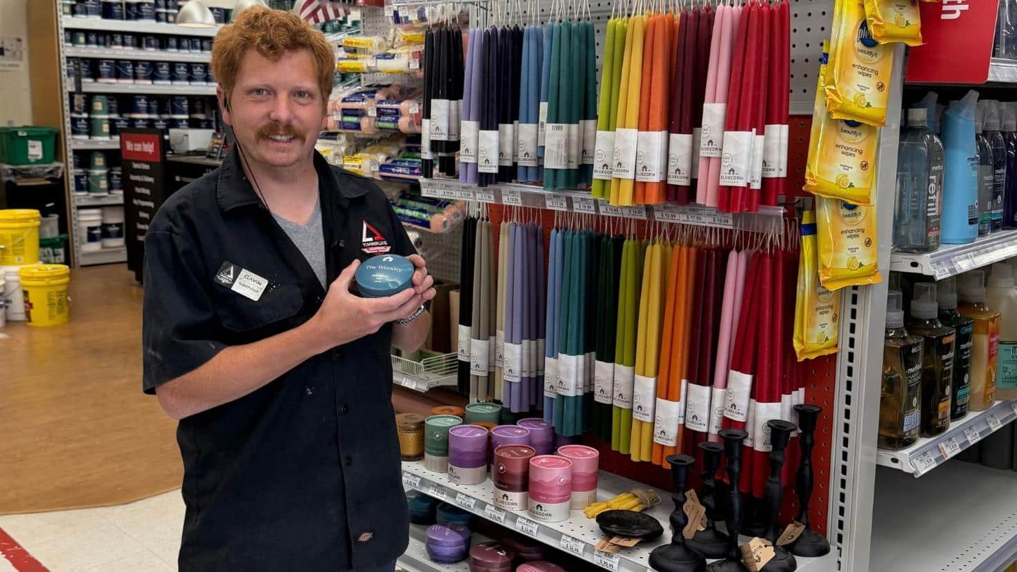 Timberline Ace team member holding a Colorado-made candle beside a colorful candle display