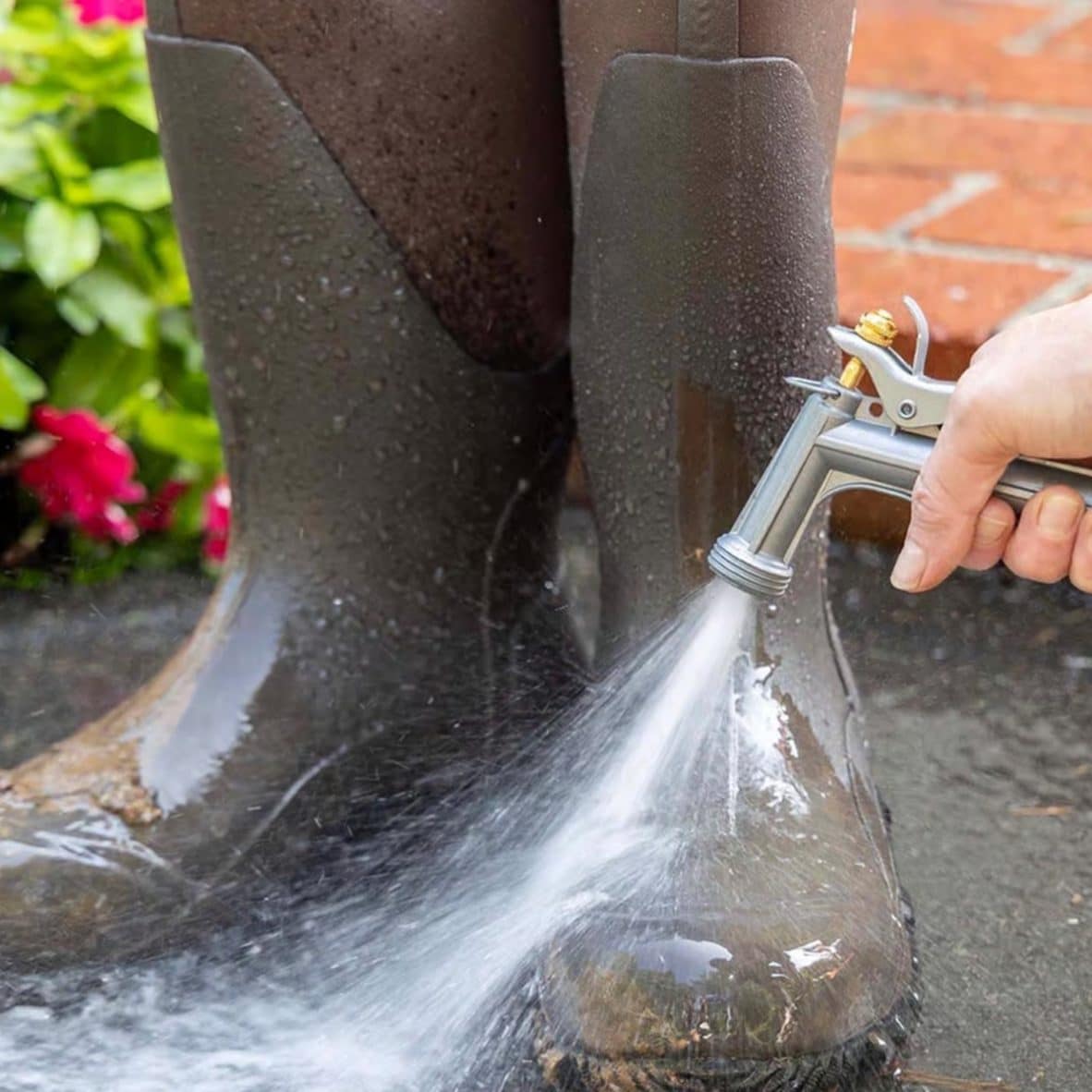 Hand holding hose nozzle spraying water on outdoor surface