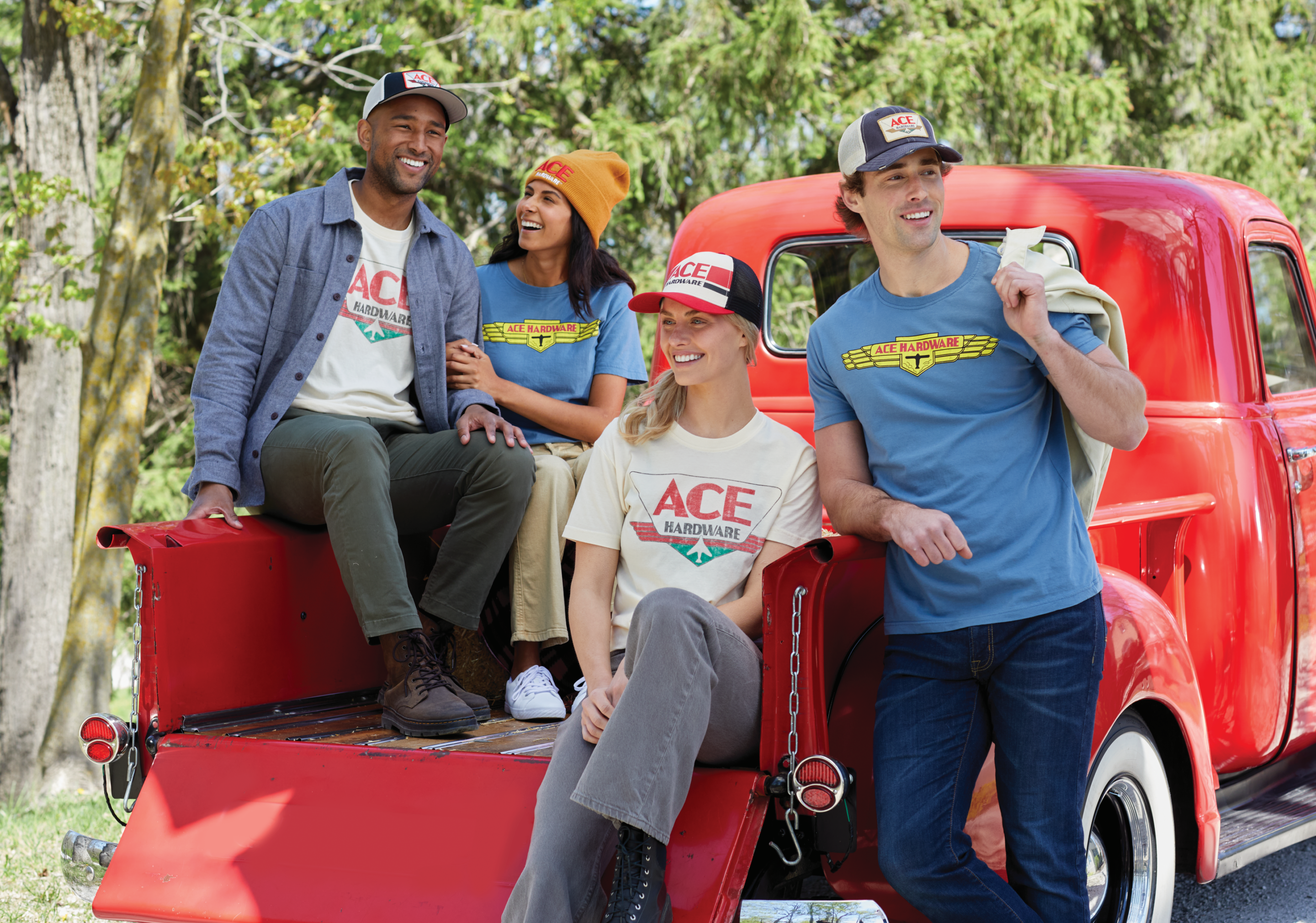 Four people wearing Ace Hardware apparel pose beside a vintage red pickup truck outdoors.